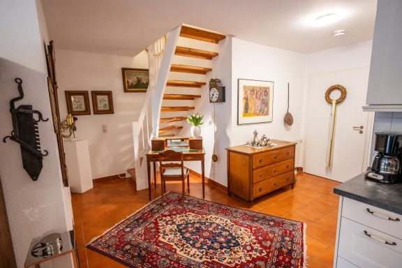 Gemütlicher Raum mit Treppe, Tisch, Stühlen und Teppich. Warme Farben, dekorative Elemente.