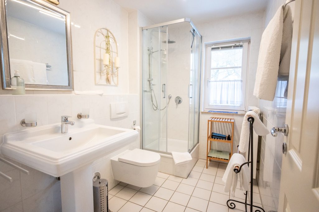 Modernes Bad mit Dusche und Glaskabine, Waschbecken, WC, Föhn, Kosmetikspiegel und Fenster. Fliegengitter sorgen für angenehmes Lüften.