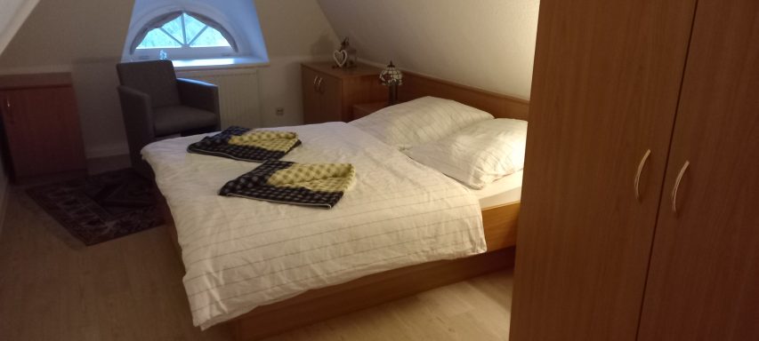 Helles Dachzimmer mit Doppelbett, Nachttisch und Schrank.