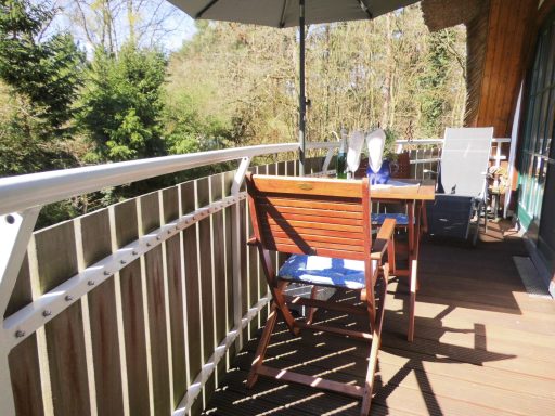 Holzstuhl auf einem Balkon, umgeben von Pflanzen und einer Sonnenschirm.