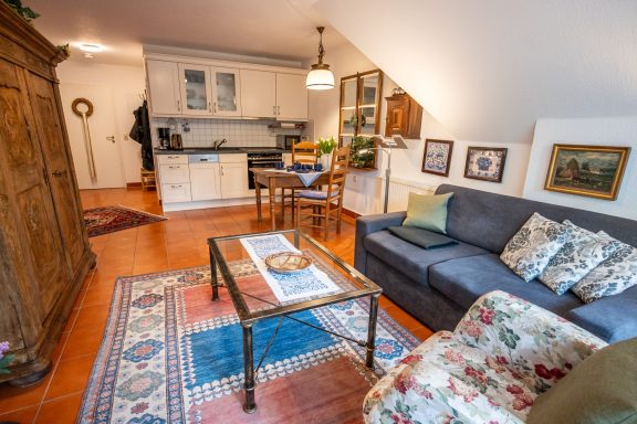 Gemütliches Wohnzimmer mit Sofa, Tisch, Küche im Hintergrund und Holzmöbeln.