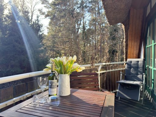 Holzstuhl auf einem Balkon, umgeben von Pflanzen und einem Sonnenschirm.