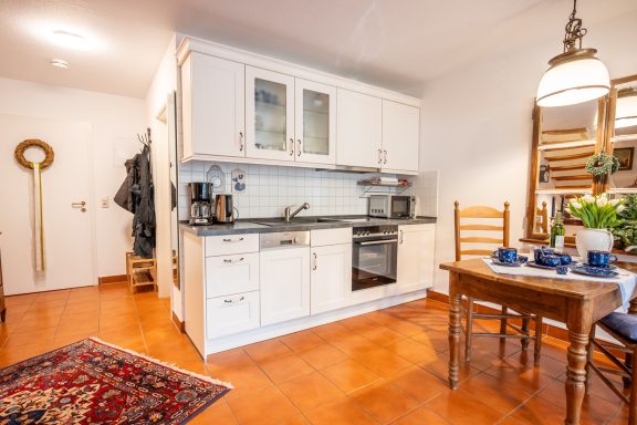 Kleine Küche mit Esstisch, Stühlen und modernen Geräten, Teppich auf dem Boden.