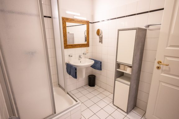 Kleines Badezimmer mit Dusche, Waschbecken, Spiegel und Schrank.