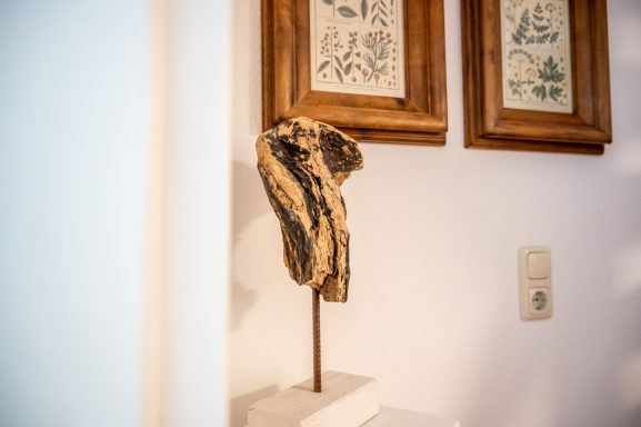 Holzskulptur auf einem Sockel, im Hintergrund gerahmte botanische Illustrationen.