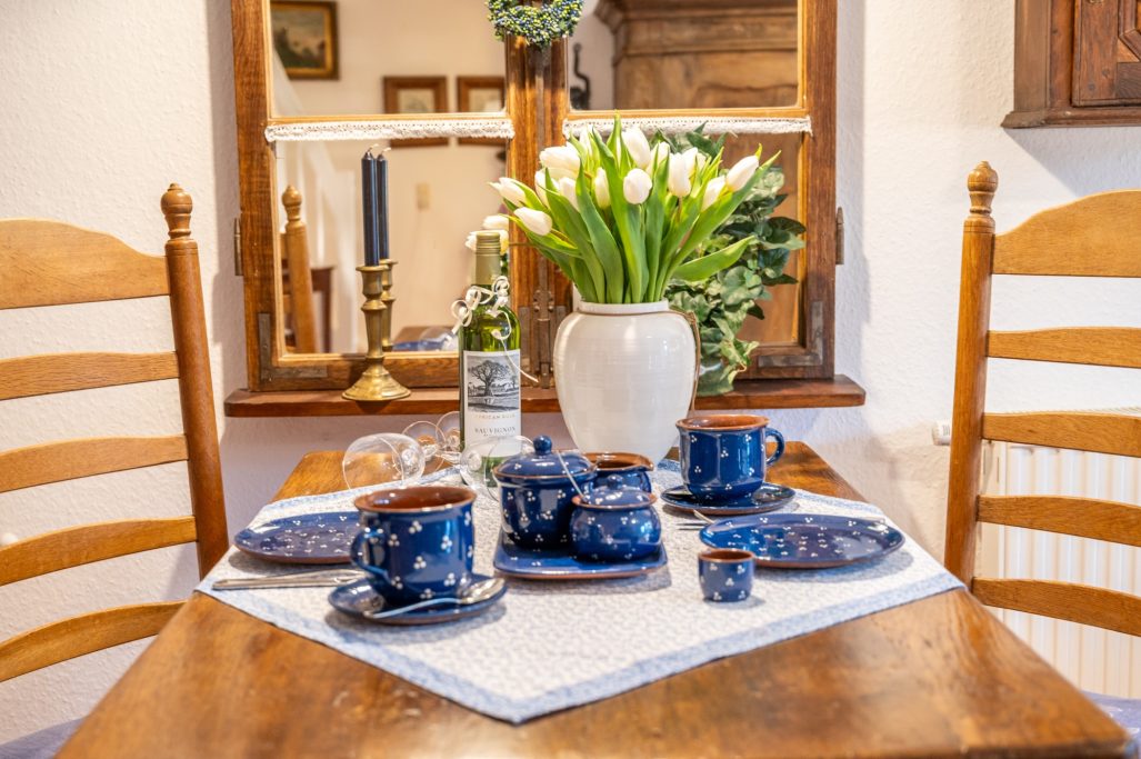 Tischgedeck mit blauen Tassen, einem weißen Vase mit Tulpen und einer Flasche Wein.
