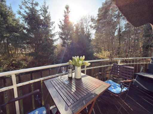 Ein Balkon mit einem Tisch und Stühlen, umgeben von Bäumen und Sonnenlicht.