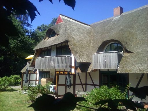 Bauernhaus mit Reetdach, Balkonen und umgeben von Grünanlagen.