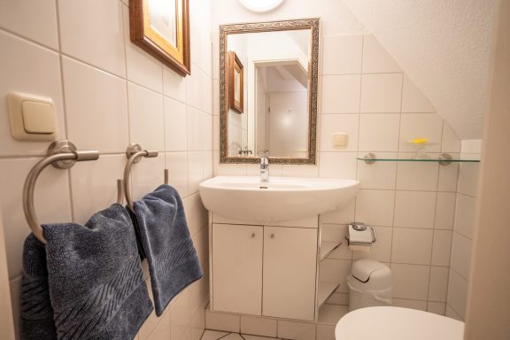 Kleines Badezimmer mit Waschbecken, Spiegel und Handtüchern an der Wand.
