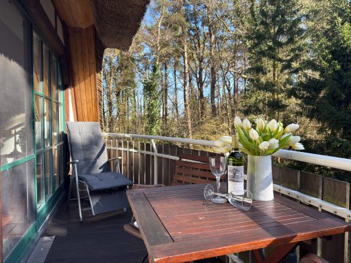 Gemütlicher Balkon mit Tisch, Stühlen, Blumen und Blick auf den Wald.