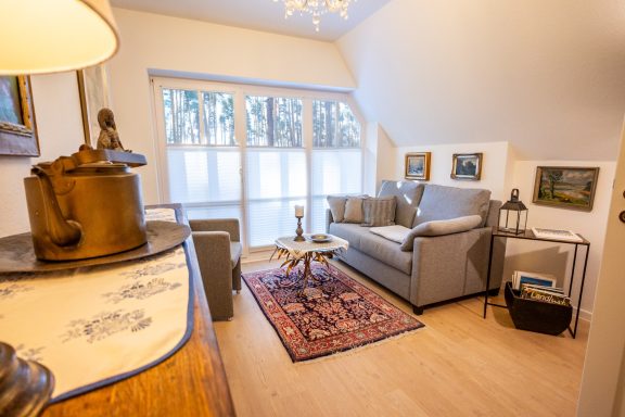 Gemütliches Wohnzimmer mit Sofa, Tisch und Kunstwerken an den Wänden. Helle Fenster.