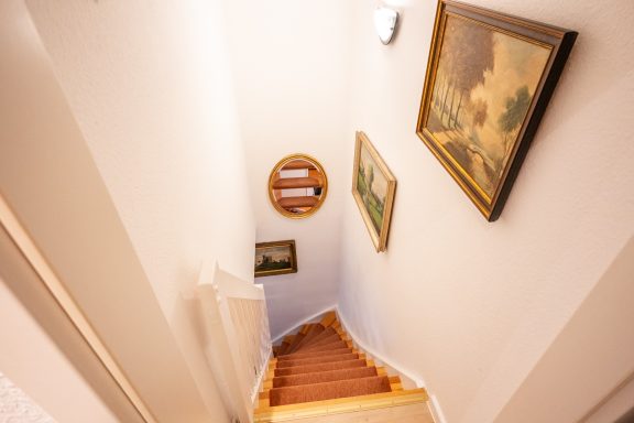 Treppe mit Holzstufen, beleuchtet, an Wänden hängen mehrere Bilder.
