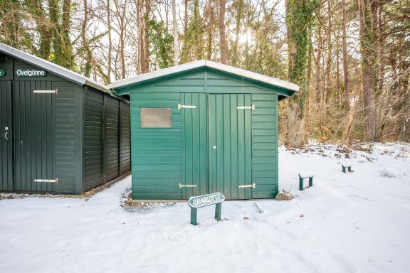 Grünes Holzhaus im Schnee, umgeben von Bäumen.